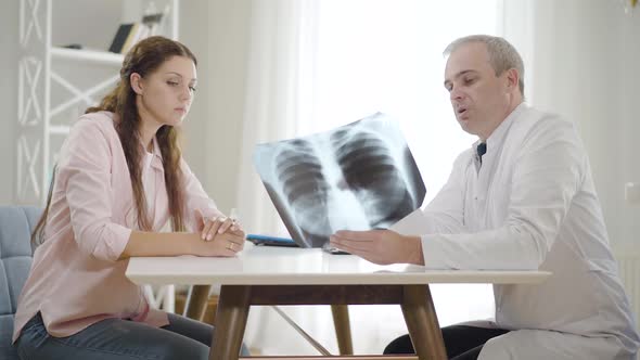 Professional Physician Explaining Lungs X-ray To Young Woman in Hospital, Side View Portrait of Mid alt