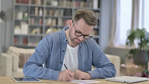 Young Man Thinking and Writing on Paper in Office alt