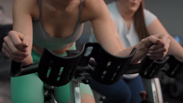 Two caucasian women ride a bikes at the gym. Shot with RED helium camera in 4K. alt