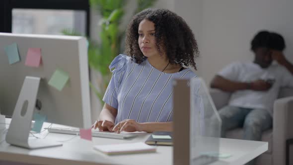 Focused African American Woman Typing Fast on Computer Keyboard with Blurred Man Surfing Internet on alt