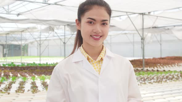 Happy Asian woman looking at camera with smiling in organic vegetable at greenhouse farm garden. alt