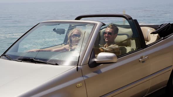 Couple driving convertible together along beach alt