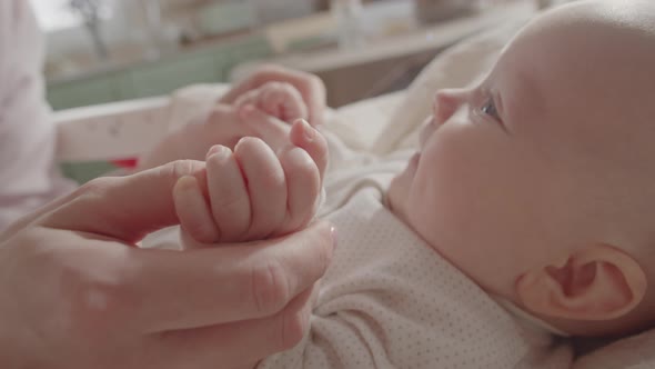 Little Baby Lying in Crib and Holding Mother Hands alt