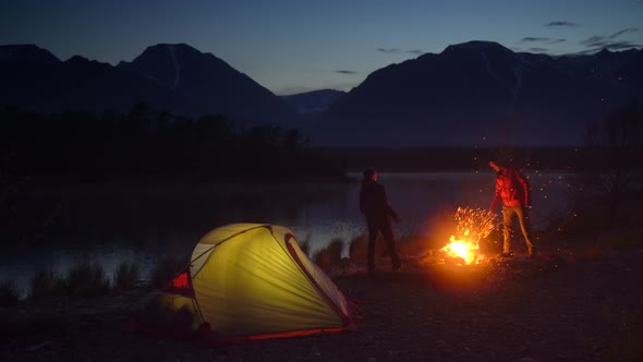 Two Tourists Camping with Tent Close to Campfire and Looking at the Mountain