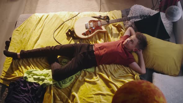 Teen Guitarist Relaxing on Bed alt
