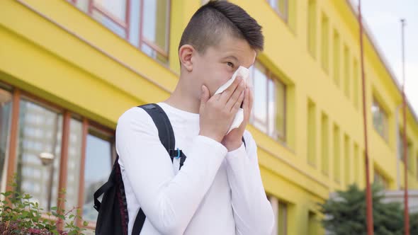 A Caucasian Teenage Boy Blows His Nose  a School in the Background