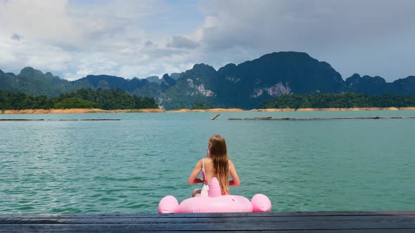 Happy Woman Have Fun and Fool Around at Pink Inflatable Flamingo on Blue Lake alt
