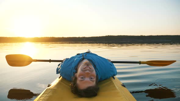 Happy Young Man Is Resting Lying on Kayak, Relaxing in Calm Lake with a Paddle  alt