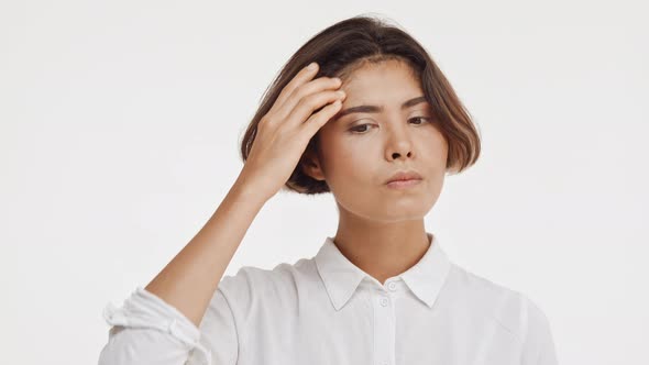 Sad Thoughtful Young Beautiful Brunette East Asian Female in Shirt Standing in Hesitation on White alt