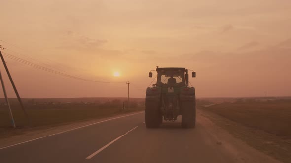 Farm tractor with large wheels driving on country road at sunset after sowing or harvesting  alt