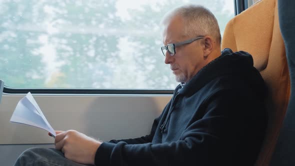 An Elderly Man on a Highspeed Train is Studying Documents While Sitting at the Window