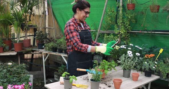 Happy latin woman working inside greenhouse garden using digital tablet alt