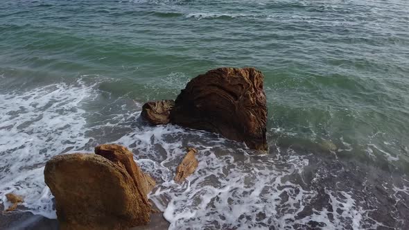Aerial view from the drone revolves around a large rock in the sea. Sea with waves beat against