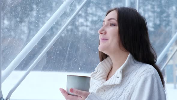 Woman Enjoys Hot Drink Looking at Winter in Panoramic Window alt