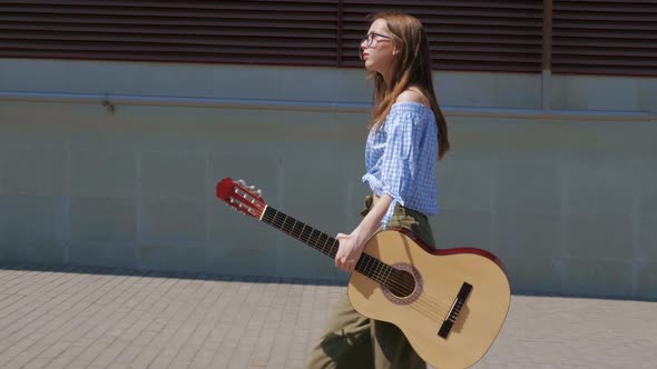 Girl with Guitar Going Past Building Wall alt