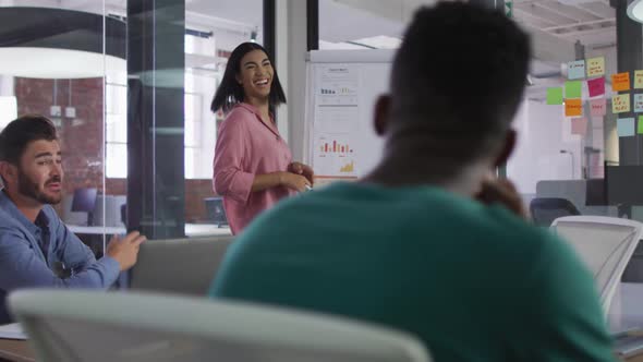 Happy mixed race businesswoman standing near white board having presentation in front of colleuagues alt