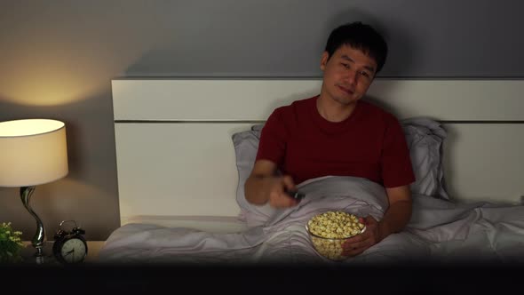 young man watching TV on a bed at night