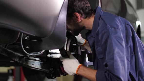 Auto Mechanic Checking Running Gear of Lifted Car alt