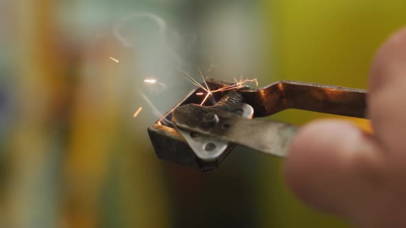 Detail of hand of a Caucasian male factory worker at a factory using a welding gun striker, sparking alt