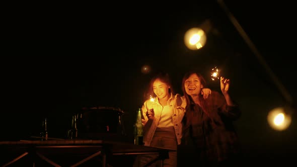 group of young Asian friends are having fun playing fireworks during a summer camping vacation.