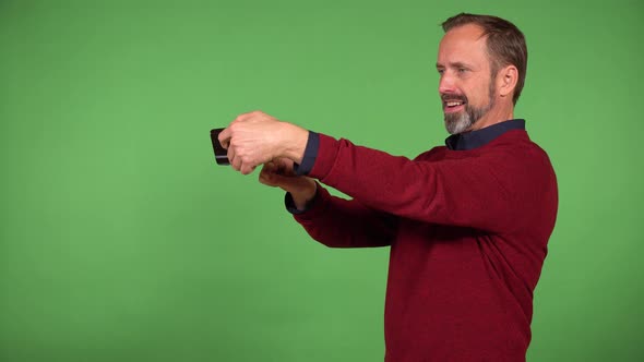 A Middleaged Handsome Caucasian Man Takes Selfies with a Smartphone  Green Screen Background