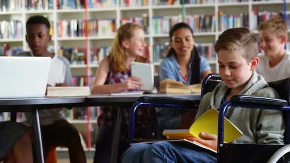 Portrait of happy schoolboy reading book on wheelchair 4k alt