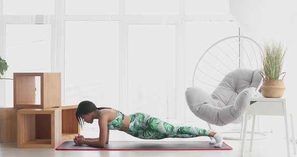 Slim black woman standing in plank position at home. alt