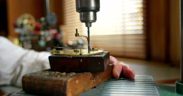 Horologist using drill machine on a clock part alt