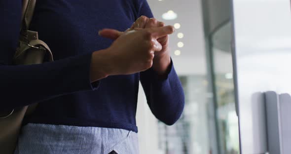 Mixed race businesswoman in face mask disinfecting hands upon arrival in office alt