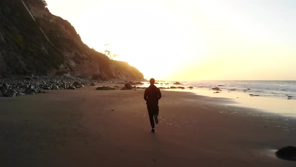 A man in silhouette running on a sand beach at sunrise during a fitness and cardio workout in Santa alt