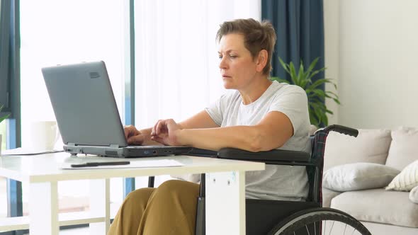 Motivated Senior Freelancer is Working Typing in Laptop Sitting in Wheelchair at Home alt