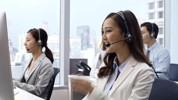 Asian woman wearing microphone headset working in customer service support help desk with colleagues