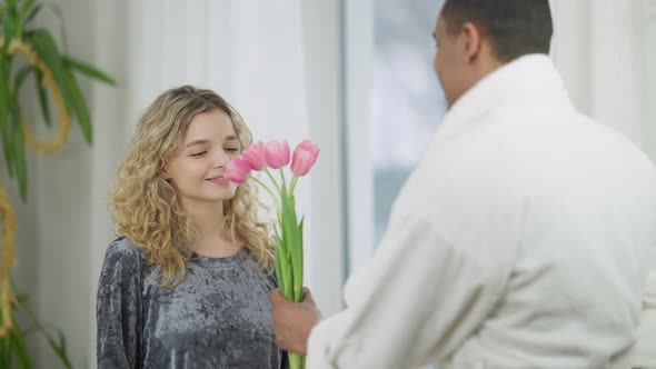 Portrait of Young Happy Woman Receiving Bouquet of Flowers in the Morning and Hugging Loving Man alt