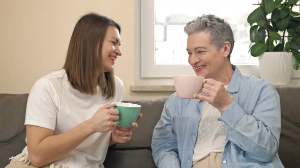 Cheerful Women of Different Ages Drink Tea or Coffee While Sitting on the Sofa in the Living Room alt