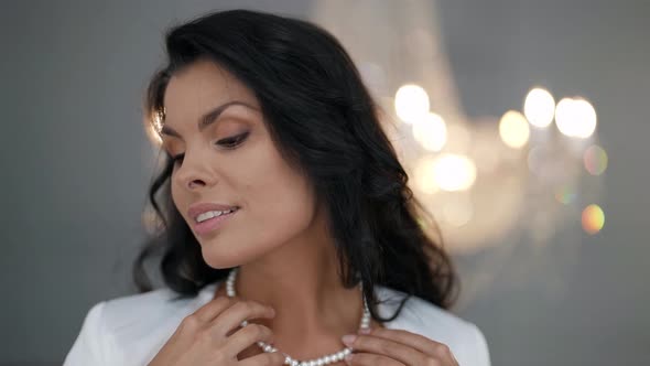 Portrait of a Brunette in a White Dress Against the Background of a Blurred Crystal Chandelier alt
