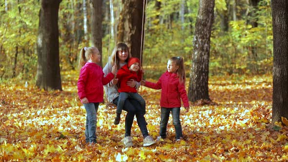 Mom swings children on a rope swing. Happy family in nature in autumn.
