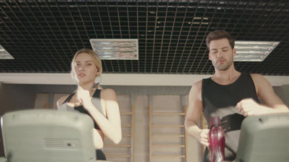 Handsome Man Flirting with Woman on Treadmill Machine in Fitness Club alt