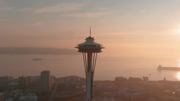 Orbiting aerial the Space Needle with a bright and smoke filled sunset over the Puget Sound in the b alt