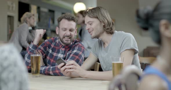 Man holding mobile phone and talking with another man in pub