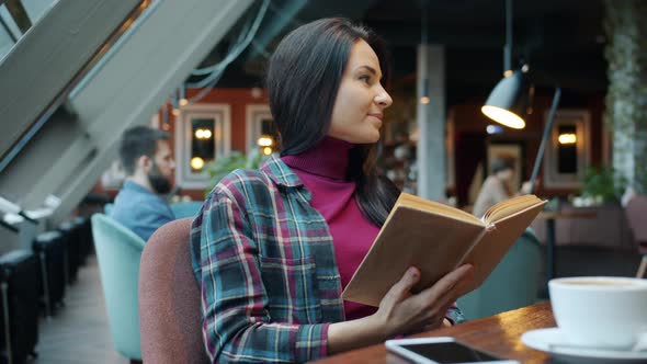 Intelligent Young Woman Reading Book Enjoying Literature Sitting at Table in Cafe alt