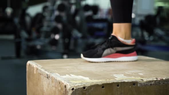 Feet of woman jumping on cube in gym