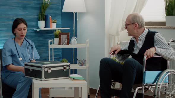 Medical Assistant Giving Bottle of Pills to Elder Man with Handicap alt