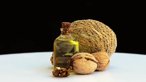 swirling walnut kernels on white background and walnut oil in bottle alt