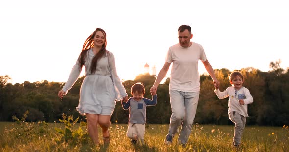 Happy Family Their Man with Two Children Walking on the Field at Sunset in the Sunset Light in the alt