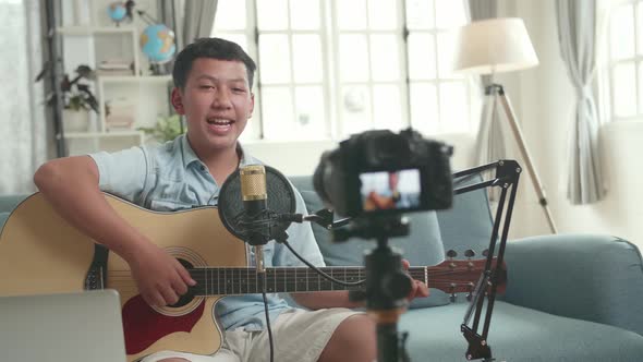Asian Boy Is A Vlogger. Boy With Guitar Talking To Camera. The Boy Is Streaming alt