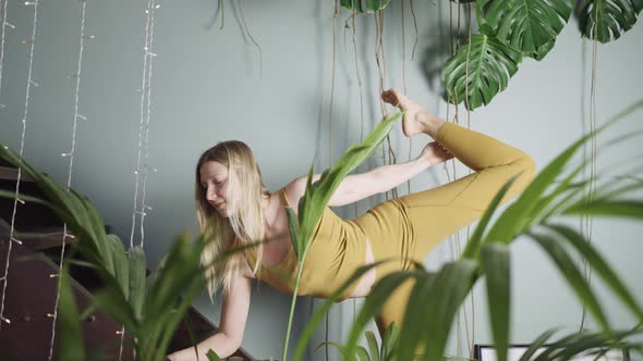 Young Woman Does Yoga Near Wooden Stairs Behind Potplant alt