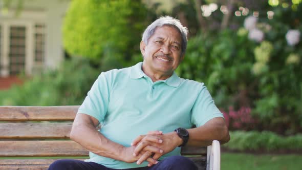Video of happy biracial senior man sitting on bench in garden alt