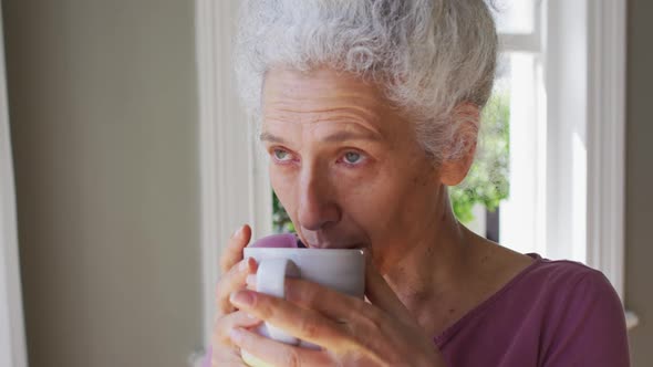 Close up of caucasian senior woman drinking coffee while looking out of the window at home alt