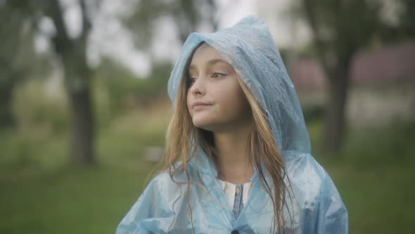 Portrait of Beautiful Caucasian Girl Standing in Raincoat Outdoors and Looking Away alt