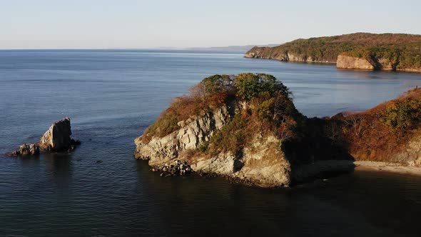 Picturesque Rocky Promontory Covered with Vegetation and Island in the Sea alt